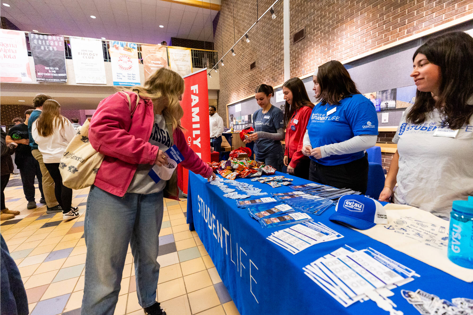 A student visits a Student Life information table on campus, where staff members hand out brochures, swag, and answer questions about campus activities and resources.